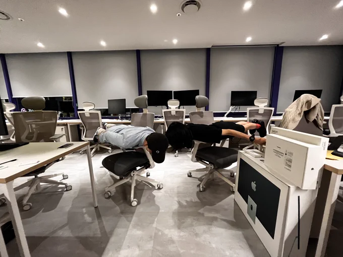 사람 두명이 의자 팔걸이에 수평으로 걸쳐 엎드려 (물리적인)수평적 업무 문화를 체험하고 있는 사진